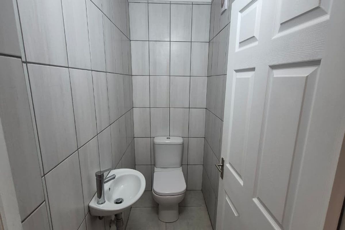 A compact, modern guest bathroom featuring floor-to-ceiling tiling, a wall-mounted basin with a mixer tap, and a standard toilet.