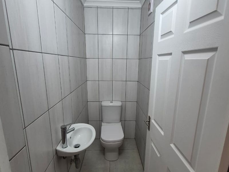 A compact, modern guest bathroom featuring floor-to-ceiling tiling, a wall-mounted basin with a mixer tap, and a standard toilet.