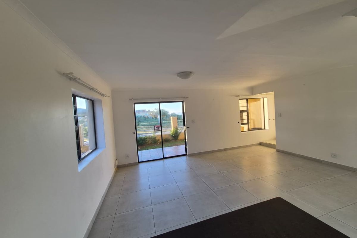 A bright, open-plan living area featuring neutral tiled flooring, large sliding glass doors leading to the exterior, and clean white walls.