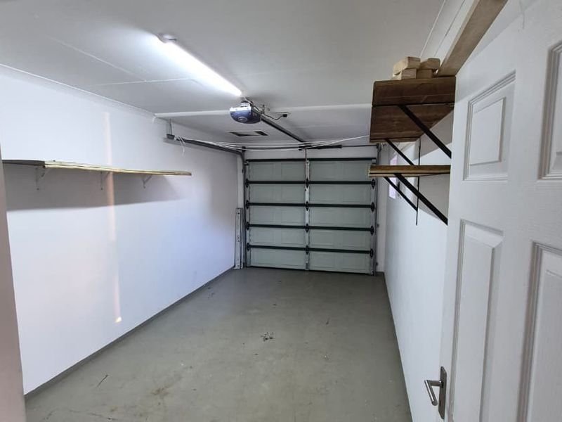 A clean, empty single-car garage featuring a sectional door, automated motor, and practical wall-mounted shelving units.