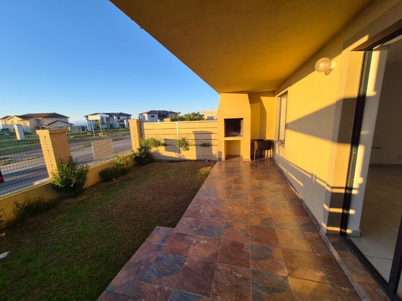 A covered patio featuring tiled flooring and a built-in braai, overlooking a small private garden and boundary wall.