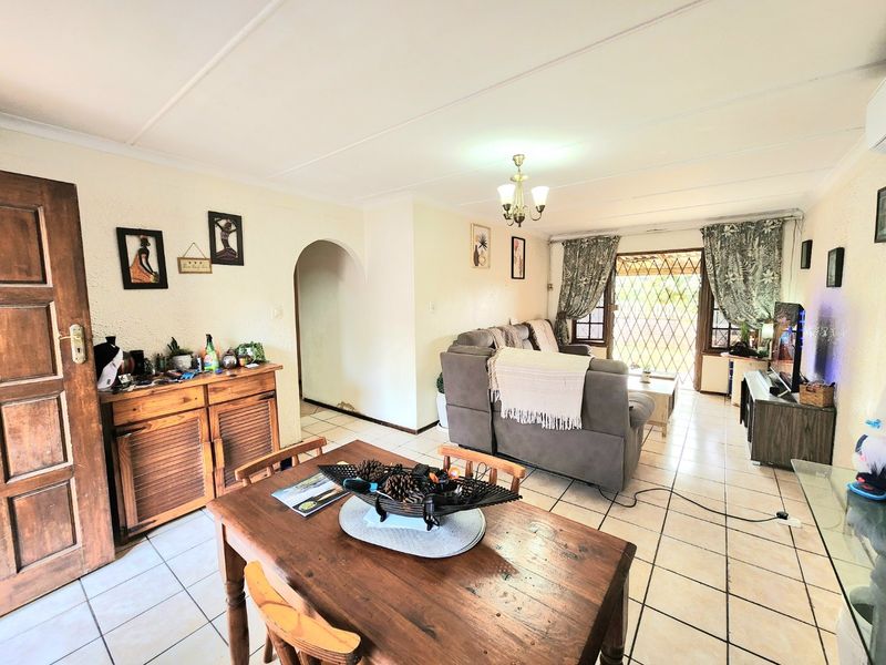 Open-plan living and dining area featuring ceramic floor tiles, an arched entryway, and direct access to the exterior through a security gate.