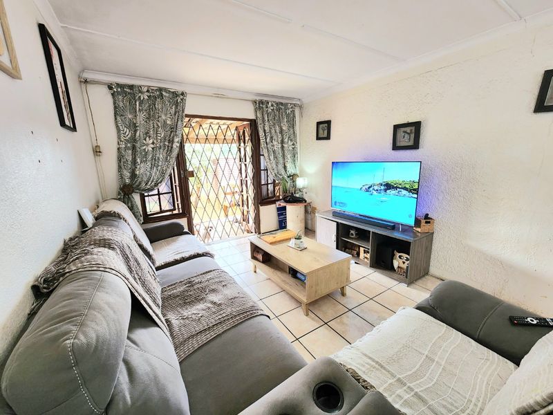 A compact living room featuring ceramic floor tiles, textured walls, and direct access to an outdoor area through a security gate and sliding door.
