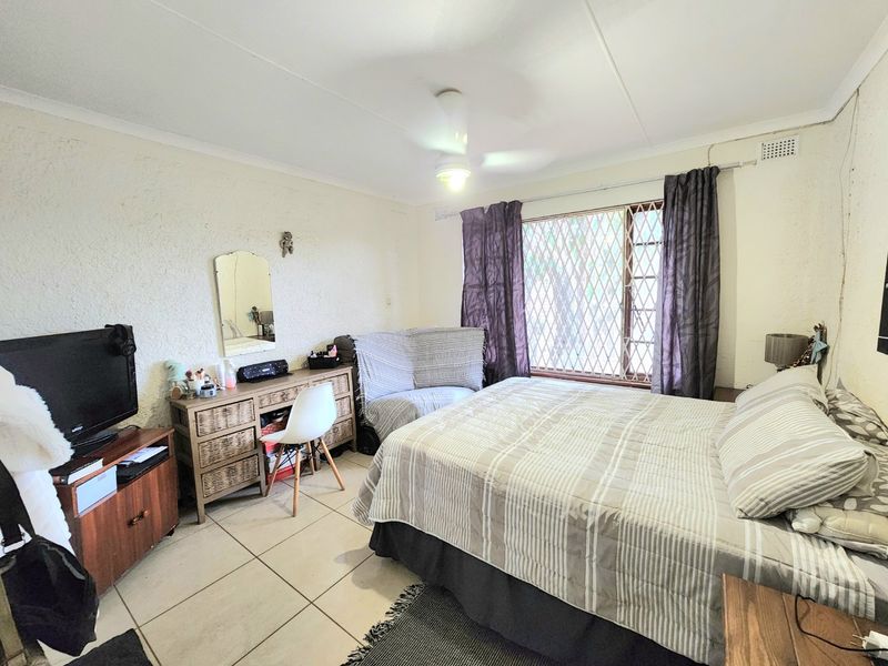 A bedroom featuring tiled flooring, a ceiling fan, and a window fitted with a security gate.