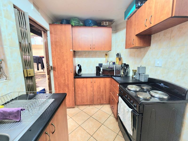 A functional kitchen featuring laminate cabinetry, black countertops, tiled backsplash, and a freestanding electric stove with direct access to an outdoor area.