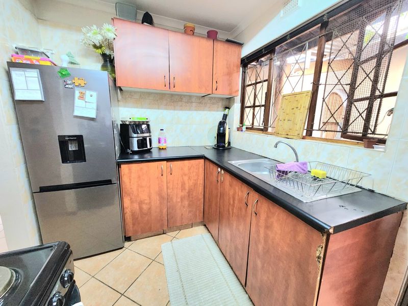 A compact kitchen featuring laminate cabinetry, dark countertops, a stainless steel sink, and tiled finishes, requiring cosmetic updates to modernize the space.