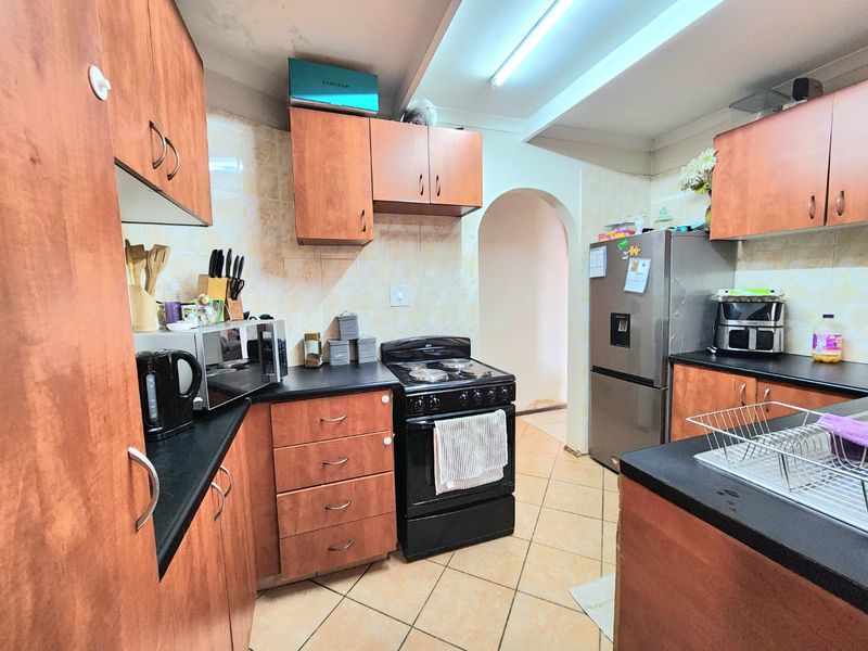 A functional kitchen featuring laminate cabinetry, dark countertops, ceramic tile backsplash, and tiled flooring, requiring cosmetic updates to modernize the space.