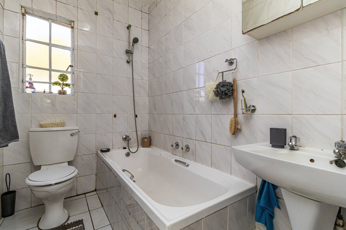 A functional bathroom featuring a bathtub with shower attachment, pedestal basin, and toilet, finished with dated wall and floor tiling.