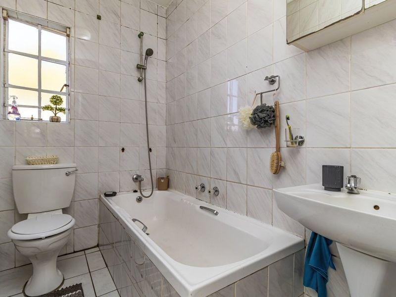 A functional bathroom featuring a bathtub with shower attachment, pedestal basin, and toilet, finished with dated wall and floor tiling.