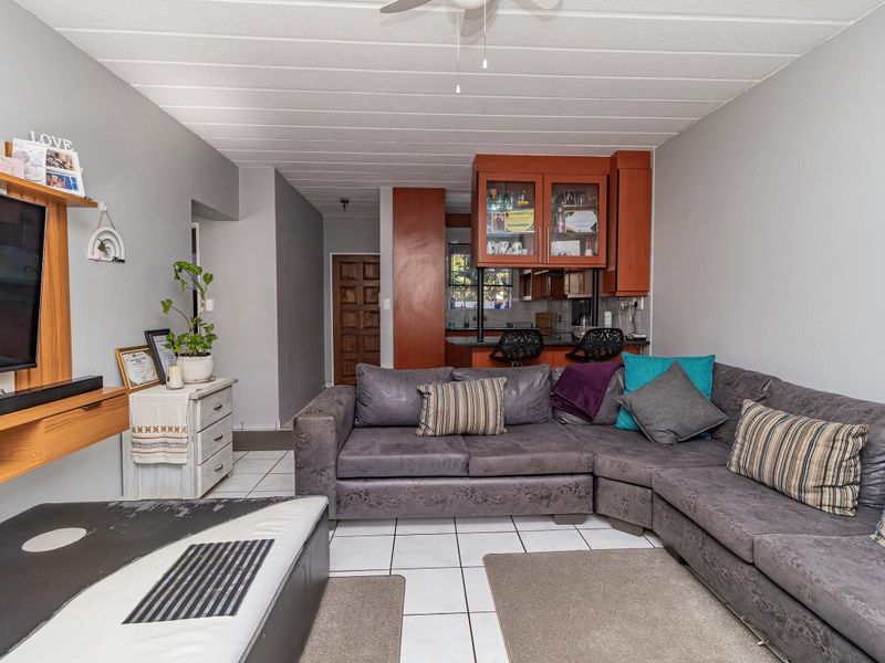 Open plan living area featuring tiled flooring, a ceiling fan, and a kitchen with built-in cabinetry and a breakfast bar.