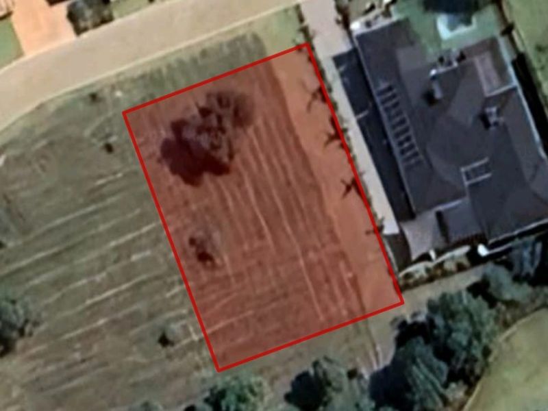 An aerial view of a vacant residential land plot with boundary markings, situated in a developed neighborhood.