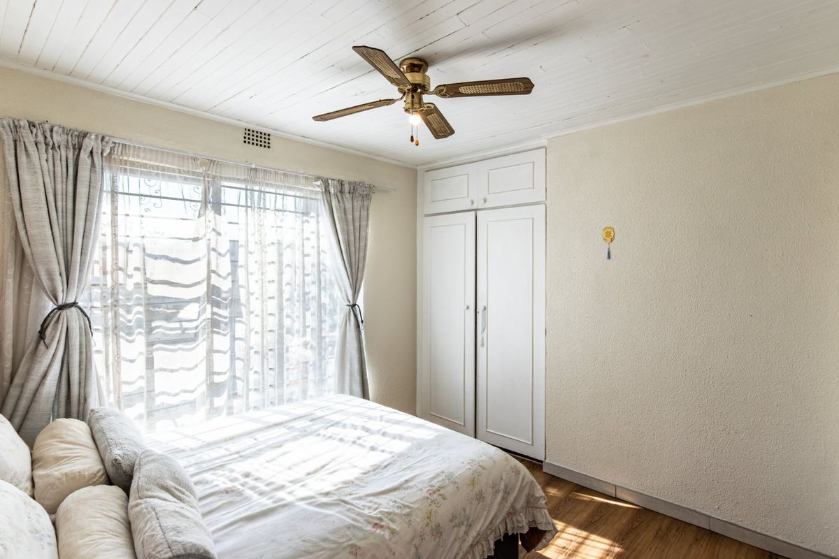 A well-lit bedroom featuring built-in cupboards, a ceiling fan, and timber flooring, offering a comfortable and functional living space.