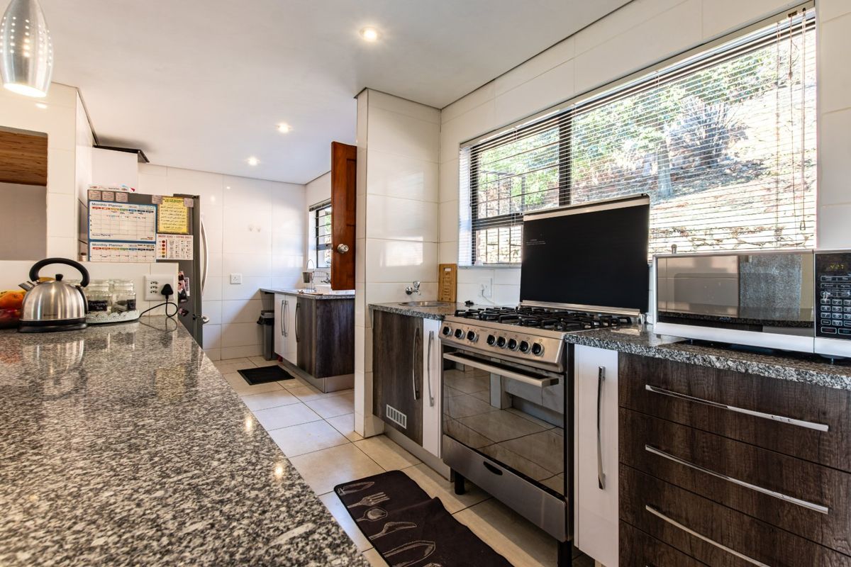 A functional kitchen featuring granite countertops, dark wood cabinetry, a gas stove, and tiled finishes throughout.