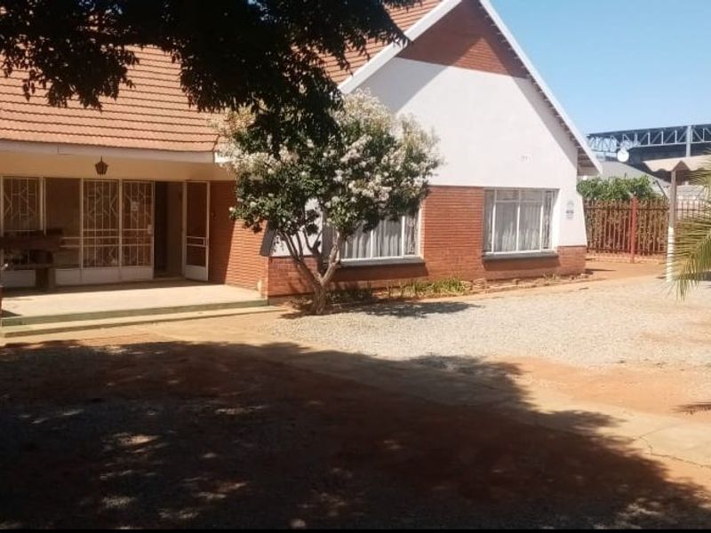 Front view of a single-story brick house featuring a tiled roof, covered porch entrance, and a spacious gravel driveway area.