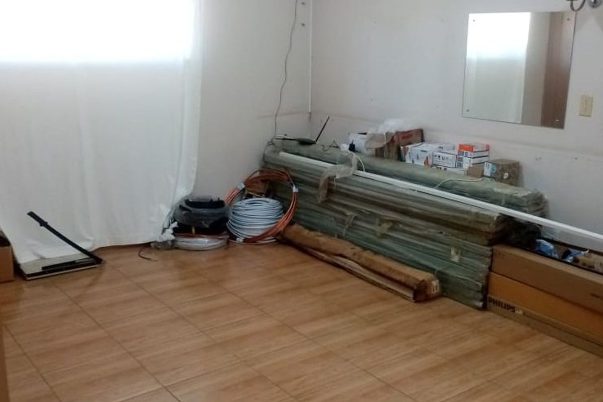An unfinished bedroom space featuring tiled flooring and wall-mounted mirrors, currently used for storage and requiring cosmetic completion.