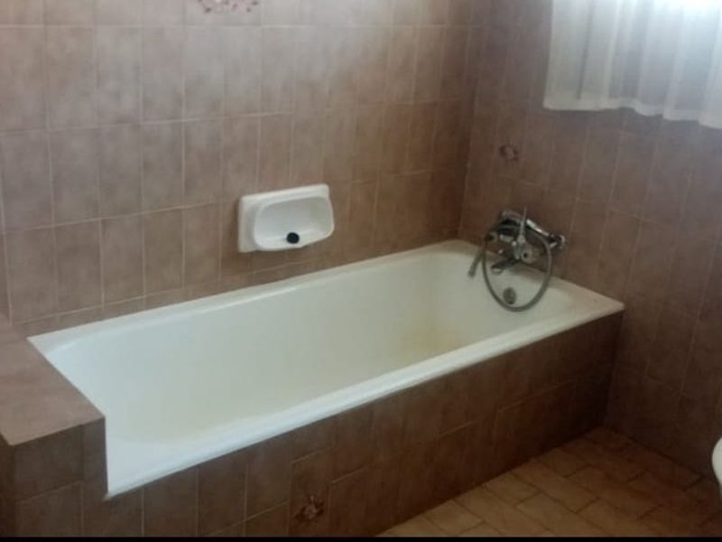 A dated bathroom featuring a built-in bathtub, tiled walls, and a vanity cabinet, requiring cosmetic updates to modernize the space.