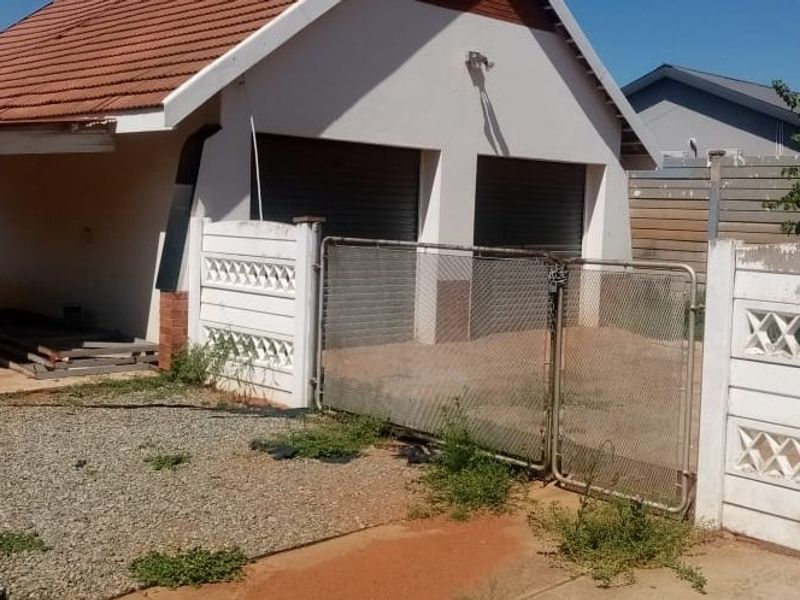 Exterior view of a double garage with roller shutter doors, featuring a precast boundary wall, metal gate, and an attached covered patio area.