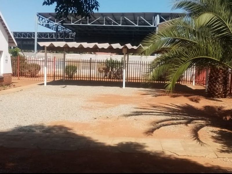 Front exterior view of the property featuring a gravel driveway, a covered carport, and perimeter metal fencing.