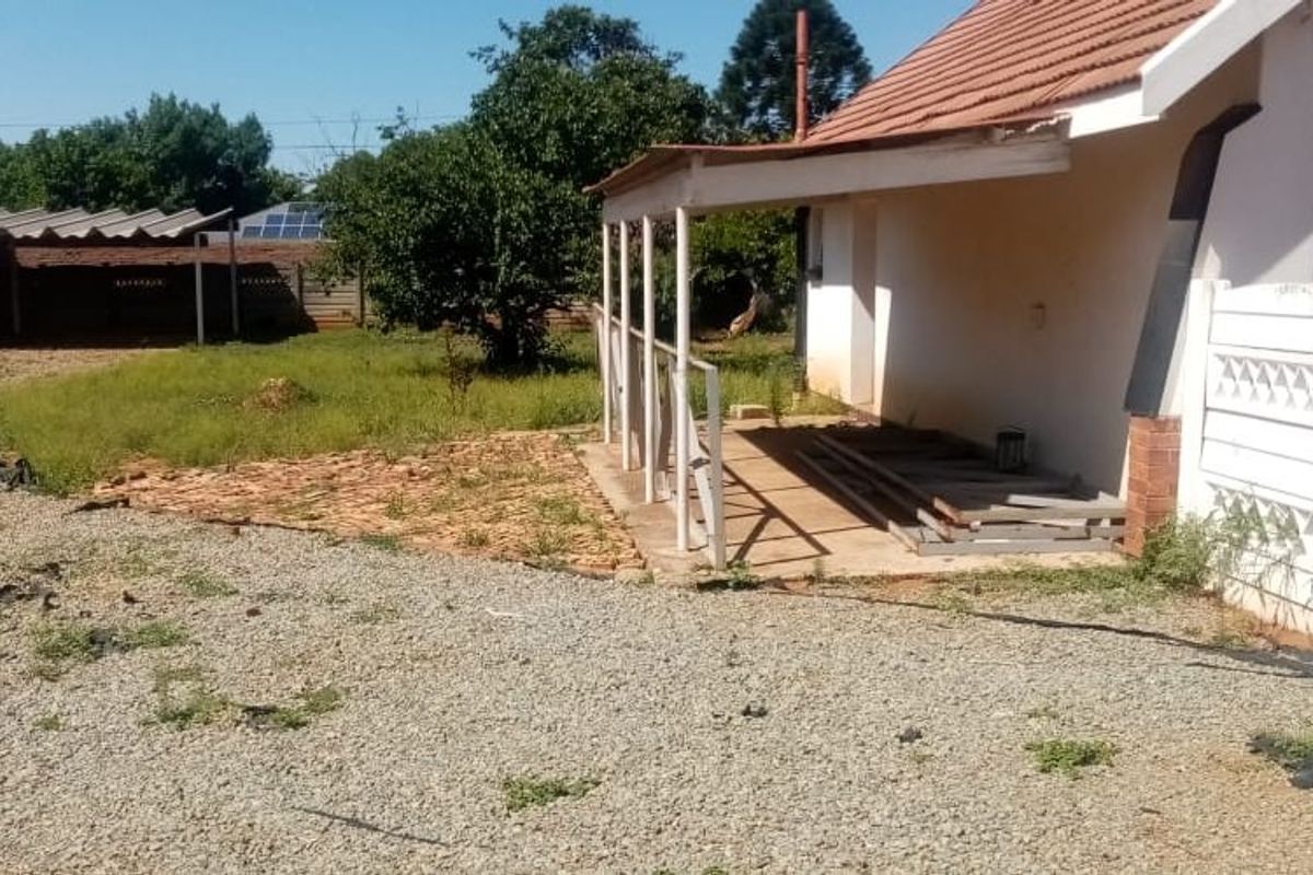 Rear exterior view of the property featuring a covered patio, gravel driveway, and a detached metal carport structure in the backyard.
