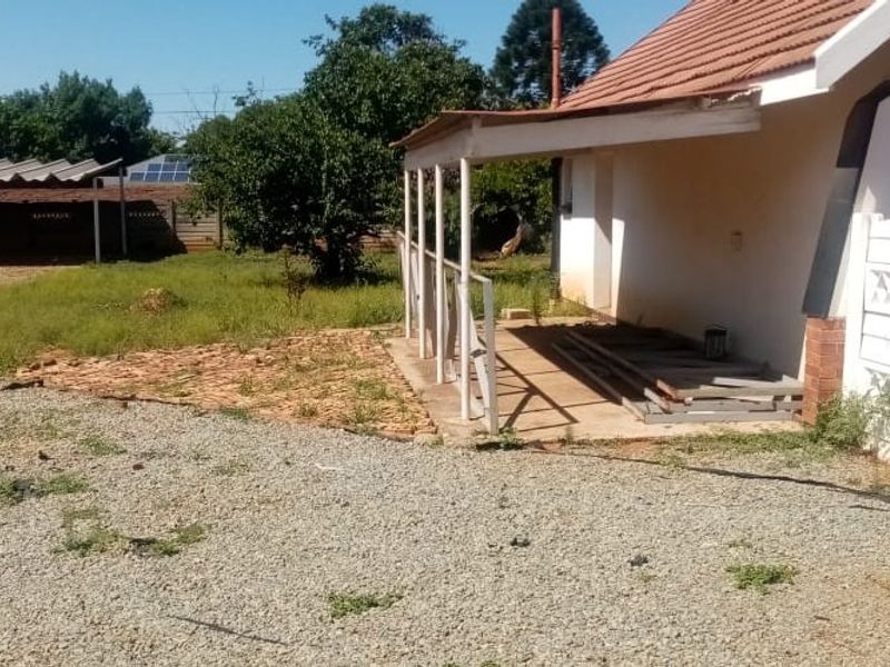 Rear exterior view of the property featuring a covered patio, gravel driveway, and a detached metal carport structure in the backyard.