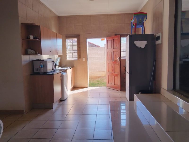 A functional kitchen featuring tiled walls and flooring, built-in cabinetry, and direct access to the rear exterior through a timber door.
