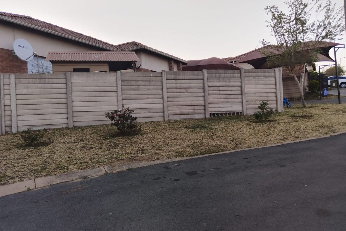 View of the rear exterior showing a precast concrete boundary wall, tiled roofline, and a small garden area.