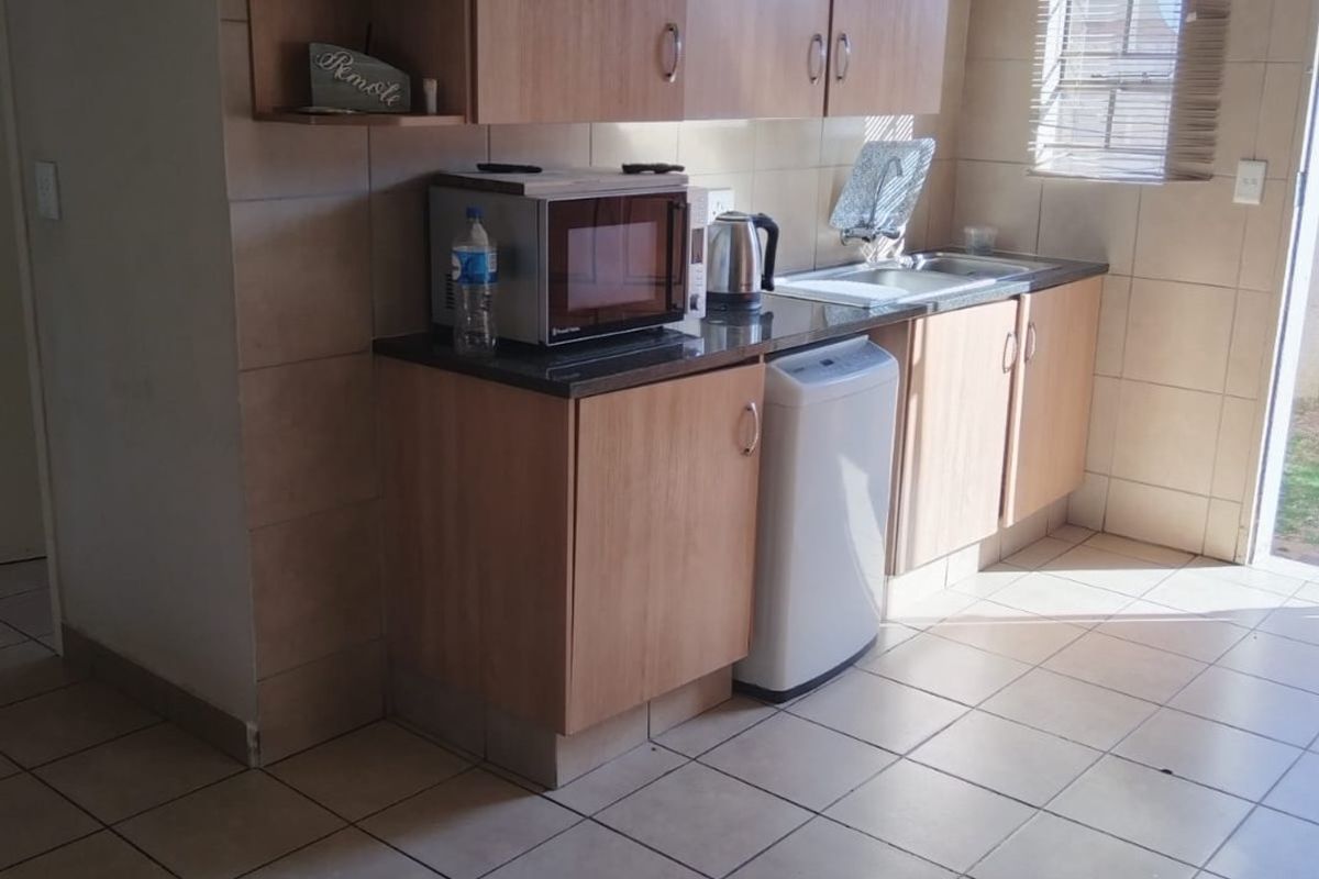A functional kitchen featuring laminate cabinetry, granite countertops, stainless steel sink, and neutral ceramic tiling throughout the floor and walls.