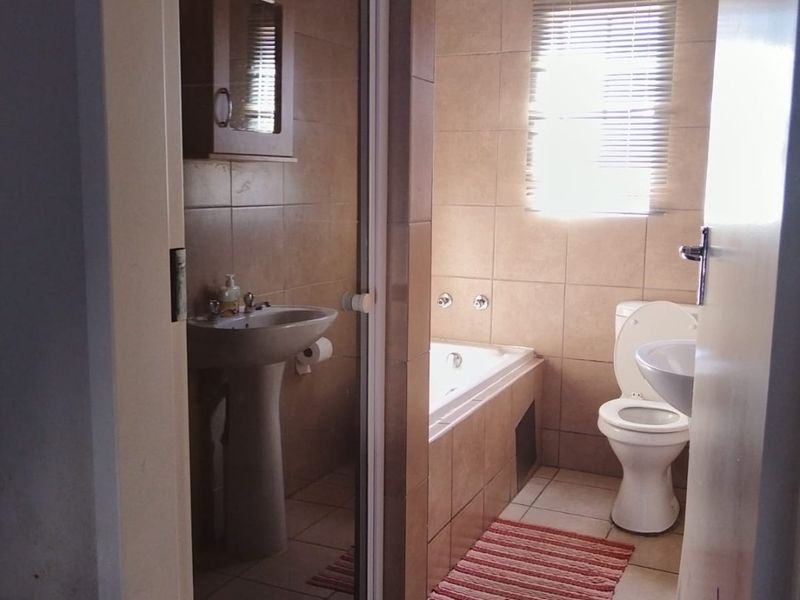 A functional bathroom featuring a pedestal basin, a built-in bathtub, a toilet, and a separate shower enclosure with tiled finishes throughout.