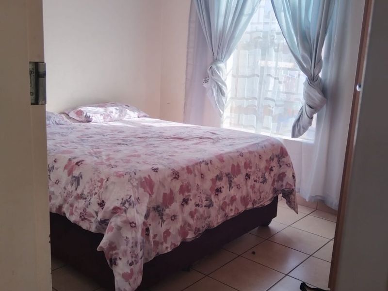 A functional bedroom featuring tiled flooring and a window with curtains, offering a simple and practical living space.