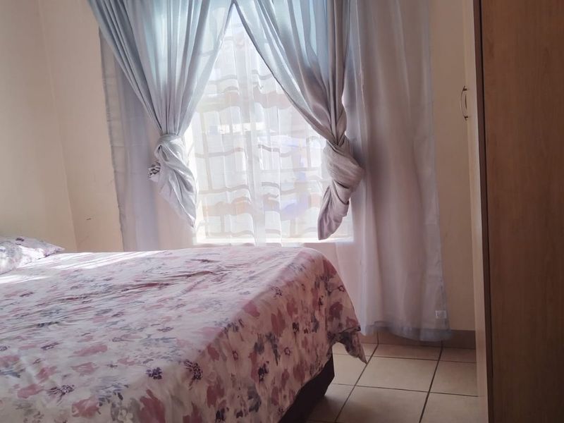 A functional bedroom featuring tiled flooring, a built-in wardrobe, and natural light through a window with curtain treatments.