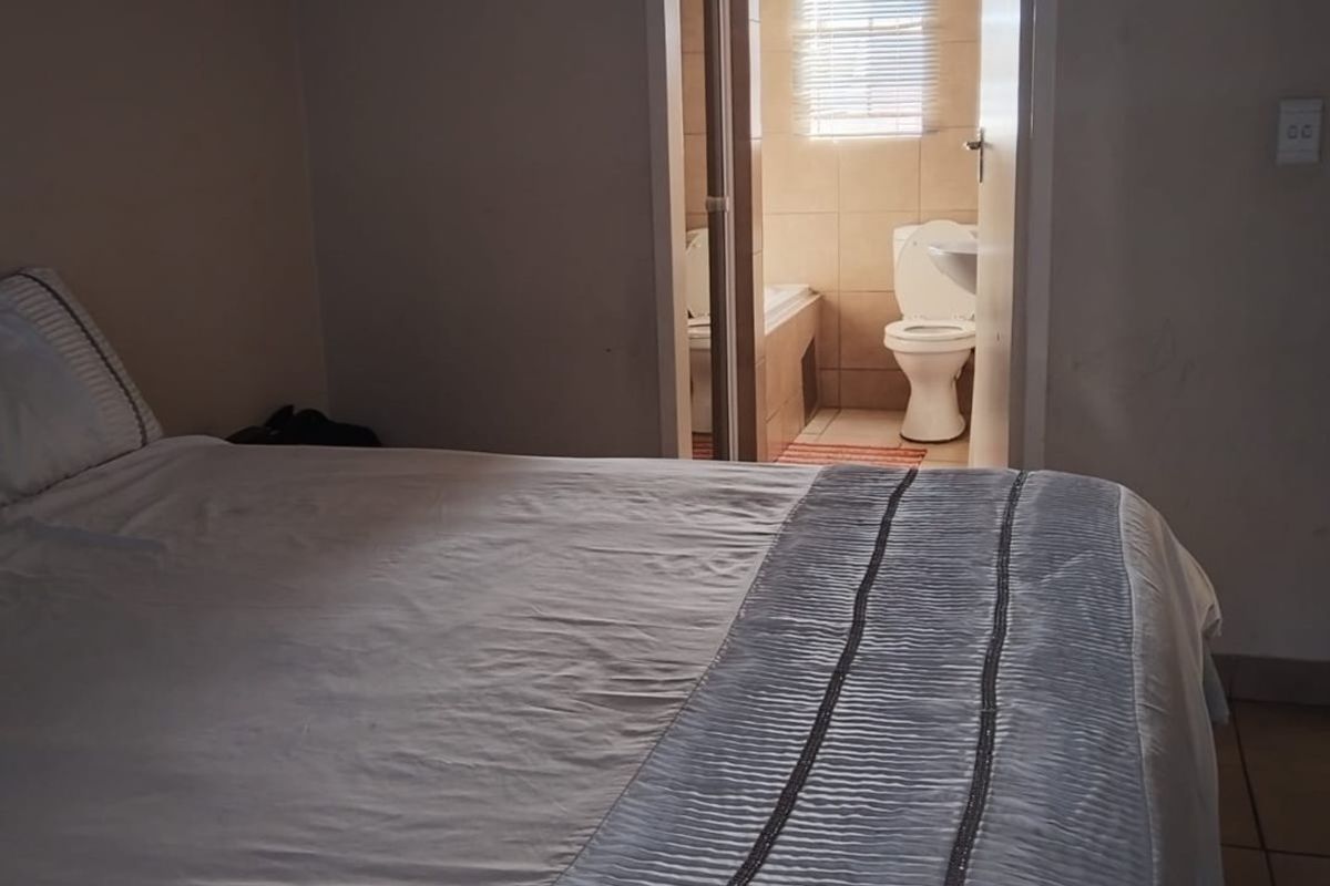 A bedroom featuring an en-suite bathroom with a bathtub and toilet, finished with neutral wall tones and tiled flooring.
