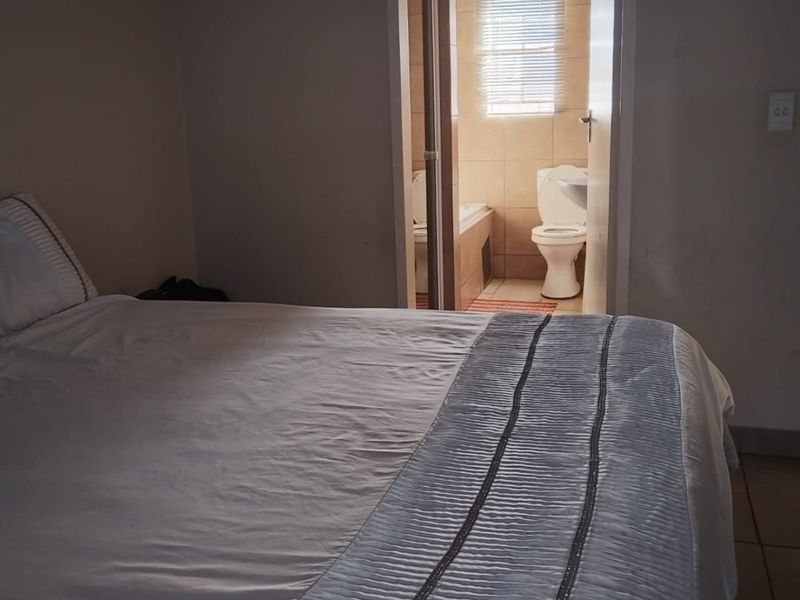 A bedroom featuring an en-suite bathroom with a bathtub and toilet, finished with neutral wall tones and tiled flooring.