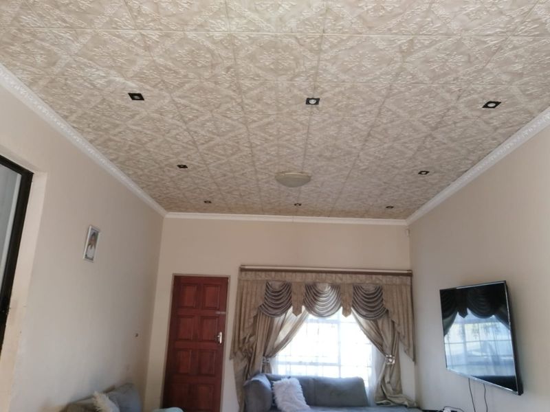 A living room featuring a textured ceiling with recessed lighting, a timber door, and a window fitted with security bars.