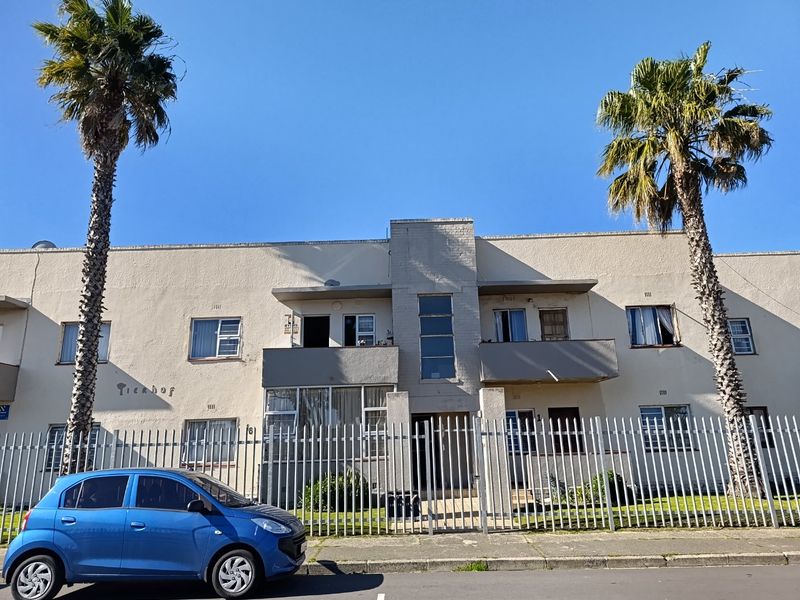Front elevation of a multi-story apartment building featuring a stucco facade, metal security fencing, and private balconies.