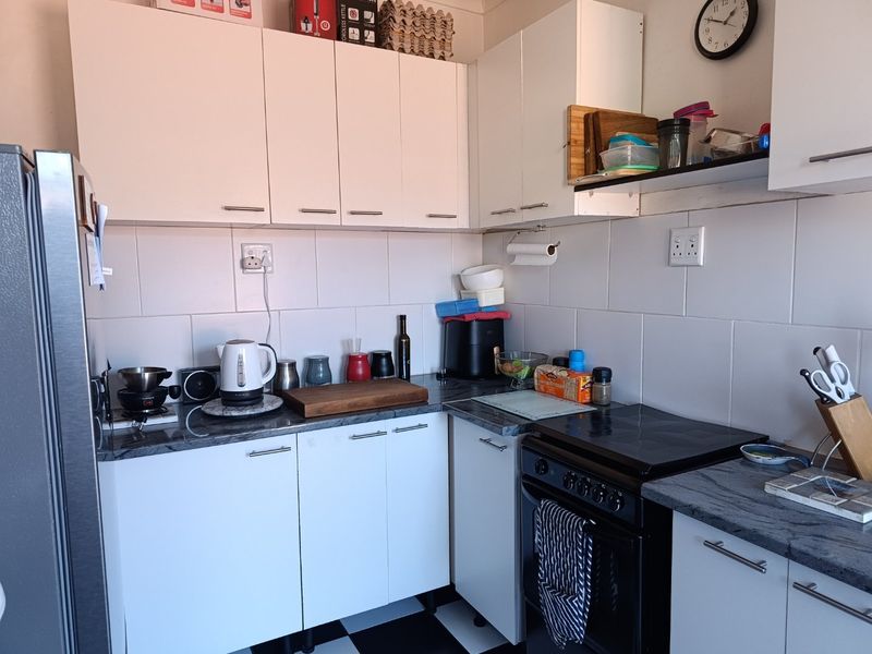 A compact kitchen featuring white cabinetry, dark laminate countertops, a tiled backsplash, and a black electric stove with checkered flooring.