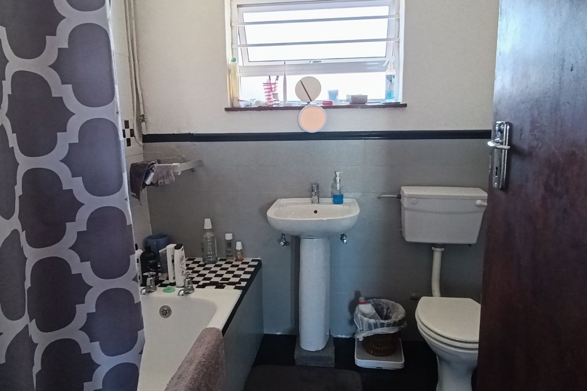 A functional bathroom featuring a pedestal basin, toilet, and bathtub with tiled splashbacks and a window for natural light.