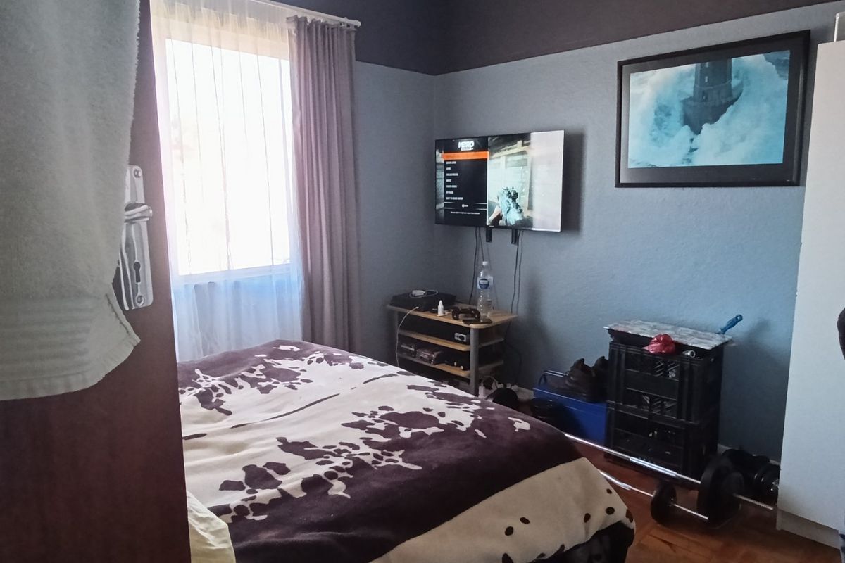 A bedroom featuring parquet flooring and a window, providing a functional space with neutral wall tones.