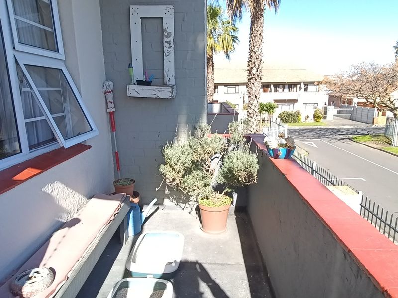 A compact apartment balcony featuring a concrete floor, painted brick wall, and metal balustrade overlooking the street.