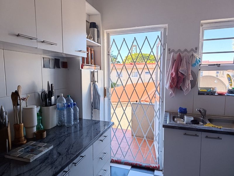 A functional kitchen featuring granite countertops, built-in cabinetry, and a stainless steel sink, with direct access to an outdoor balcony area.