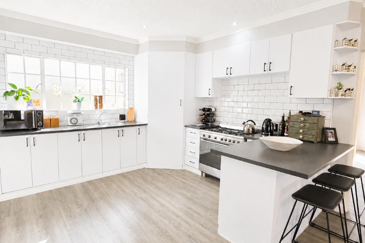Modern kitchen featuring white cabinetry, subway tile backsplash, a central island with breakfast bar seating, and durable laminate flooring.