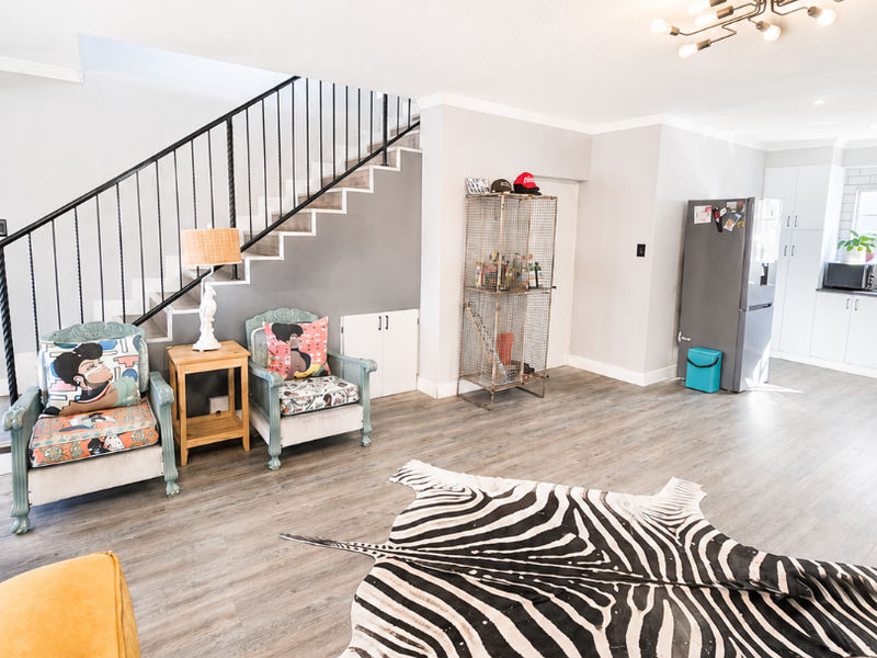 Spacious open-plan living area featuring a modern staircase with metal balustrade, light-toned laminate flooring, and integrated kitchen cabinetry.