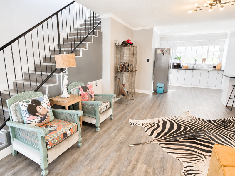 Open plan living area featuring a staircase with metal balustrade, flowing into a modern kitchen with white cabinetry and subway tile backsplash.