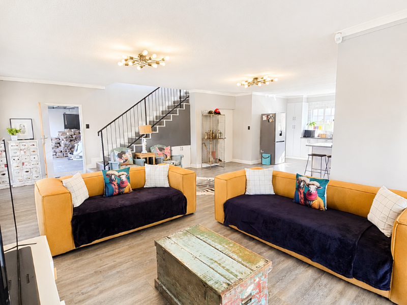 Spacious open-plan living area featuring modern laminate flooring, a central staircase with metal balustrade, and a seamless transition into the kitchen space.
