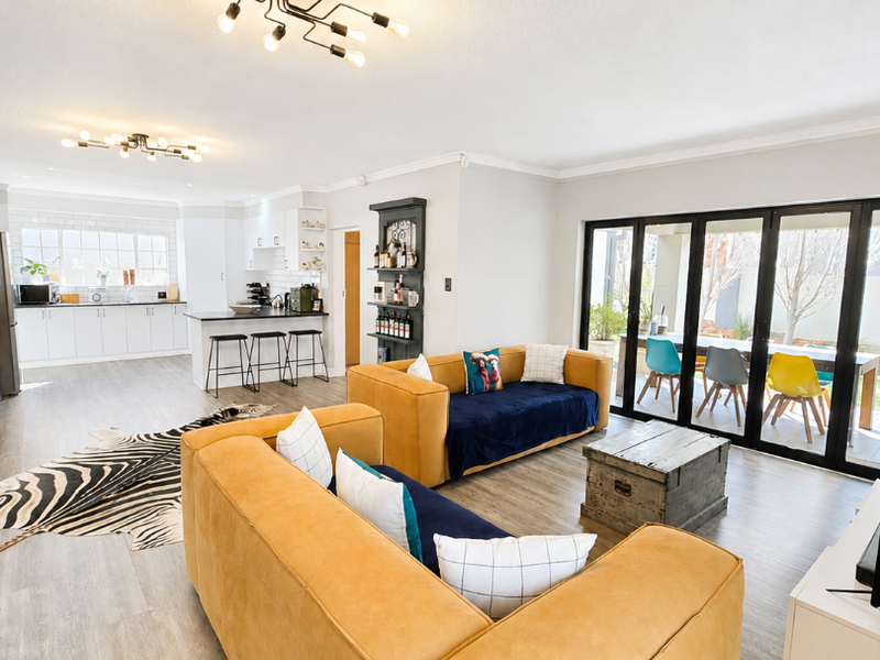 Spacious open-plan living area featuring a modern kitchen with island, light laminate flooring, and large bi-fold doors opening to an outdoor patio.