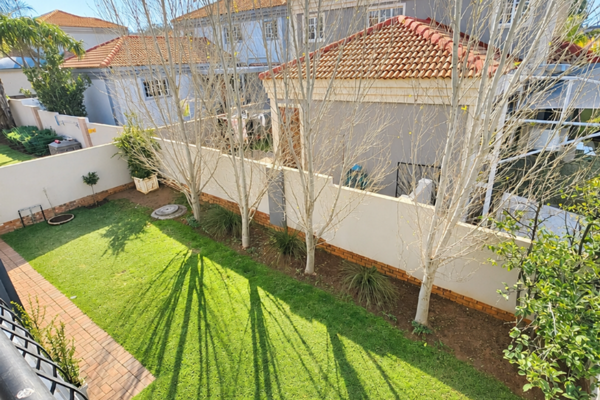 A view of the rear garden featuring a well-maintained lawn, paved pathway, and boundary wall, viewed from an elevated position.