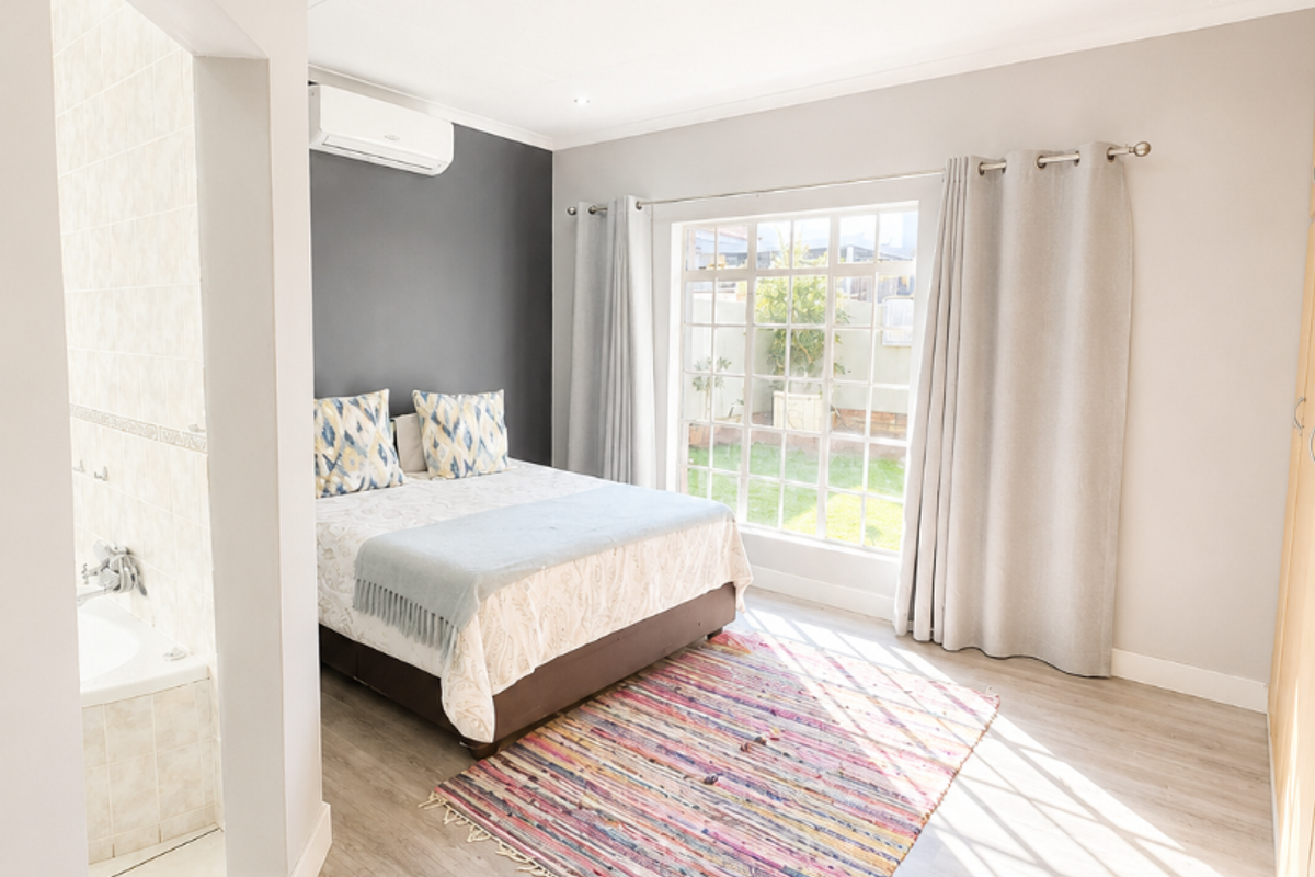 Bright bedroom featuring laminate flooring, an en-suite bathroom, built-in cupboards, and an air conditioning unit, with direct access to natural light.