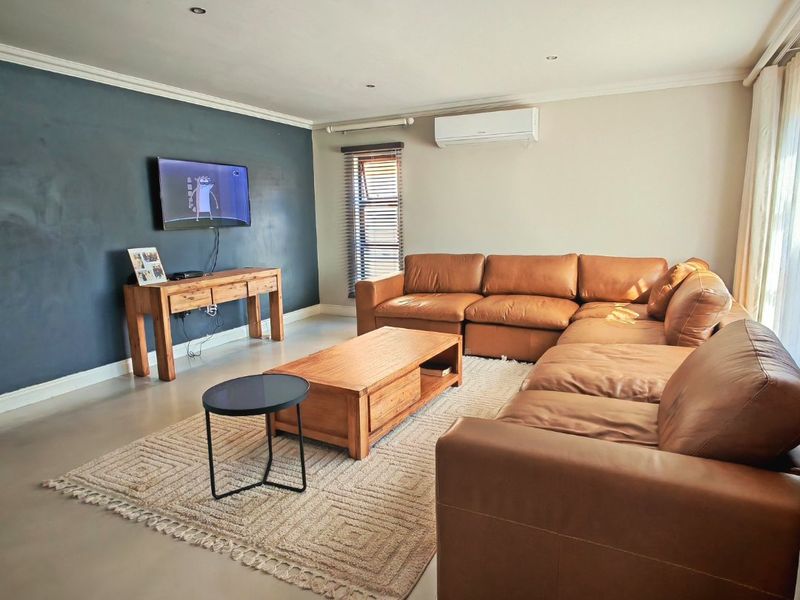 A comfortable living room featuring polished concrete floors, recessed lighting, a wall-mounted air conditioning unit, and a feature wall.