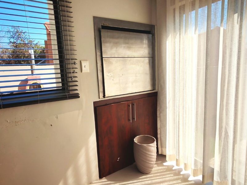 A bright living area featuring a built-in indoor braai, dark wood cabinetry, and large windows with venetian blinds and curtain tracks.