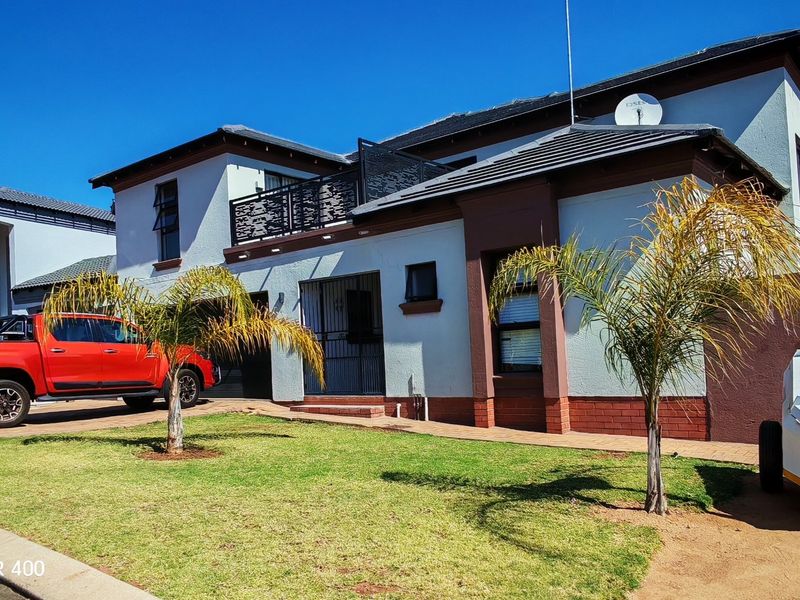 Front elevation of a two-story residential house featuring a tiled roof, balcony with decorative metal railing, and a paved driveway.