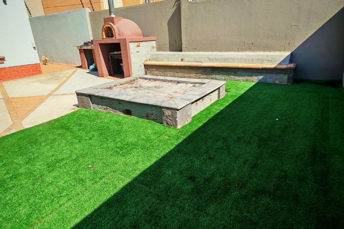 Rear garden area featuring a built-in pizza oven, fire pit, and integrated bench seating with artificial lawn and paved patio space.